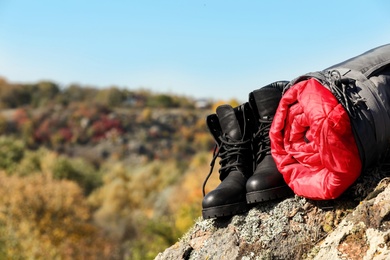 Photo of Boots and sleeping bag on rock outdoors, space for text. Camping equipment