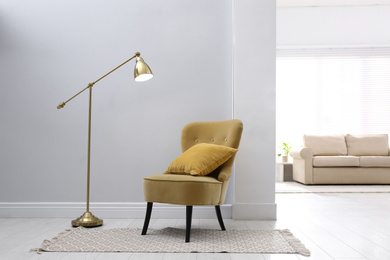 Photo of Comfortable armchair with cushion, rug and lamp indoors