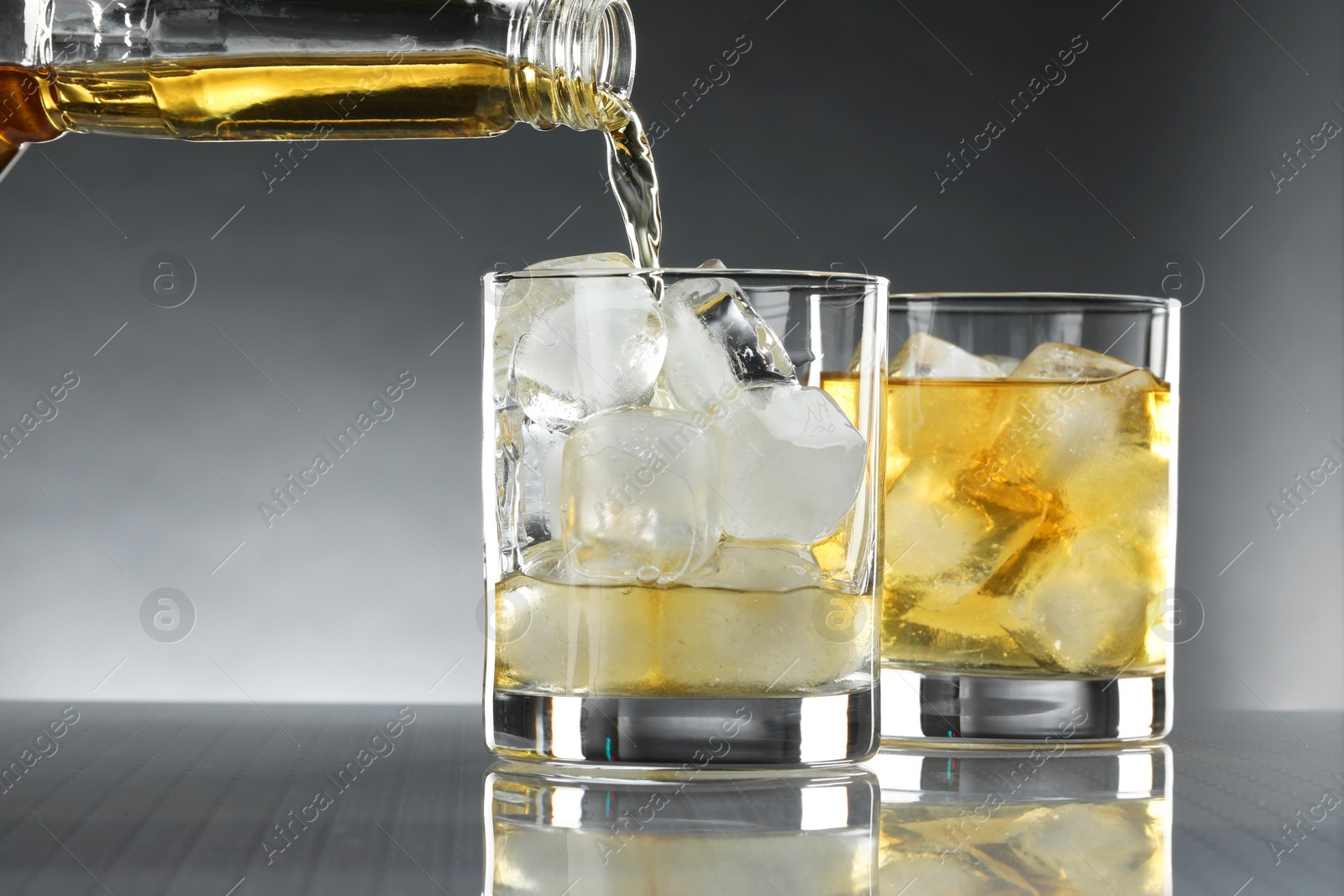 Photo of Pouring tasty whiskey from bottle into glass at mirror table, closeup