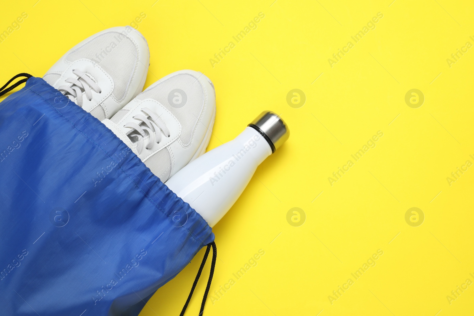 Photo of Blue drawstring bag, thermo bottle and sneakers on yellow background, above view. Space for text
