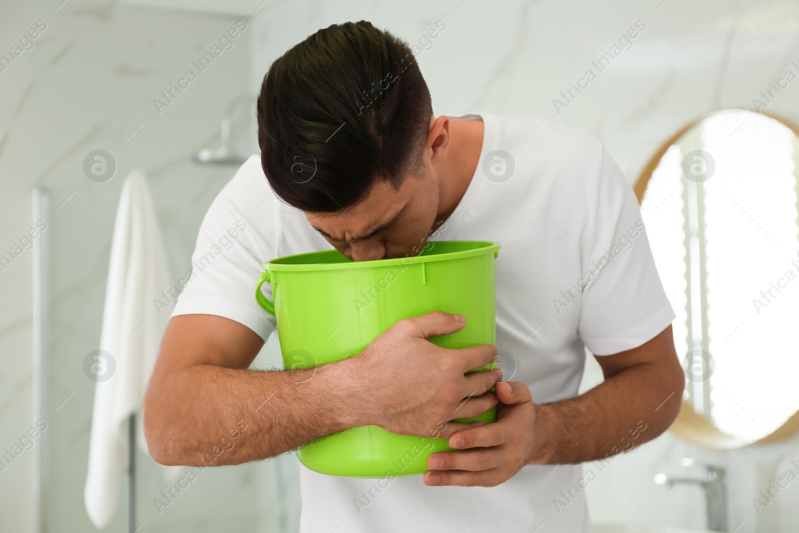 Photo of Man with bucket suffering from nausea in bathroom. Food poisoning