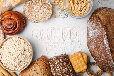 Different products and phrase Gluten free written with flour on white tiled table, flat lay