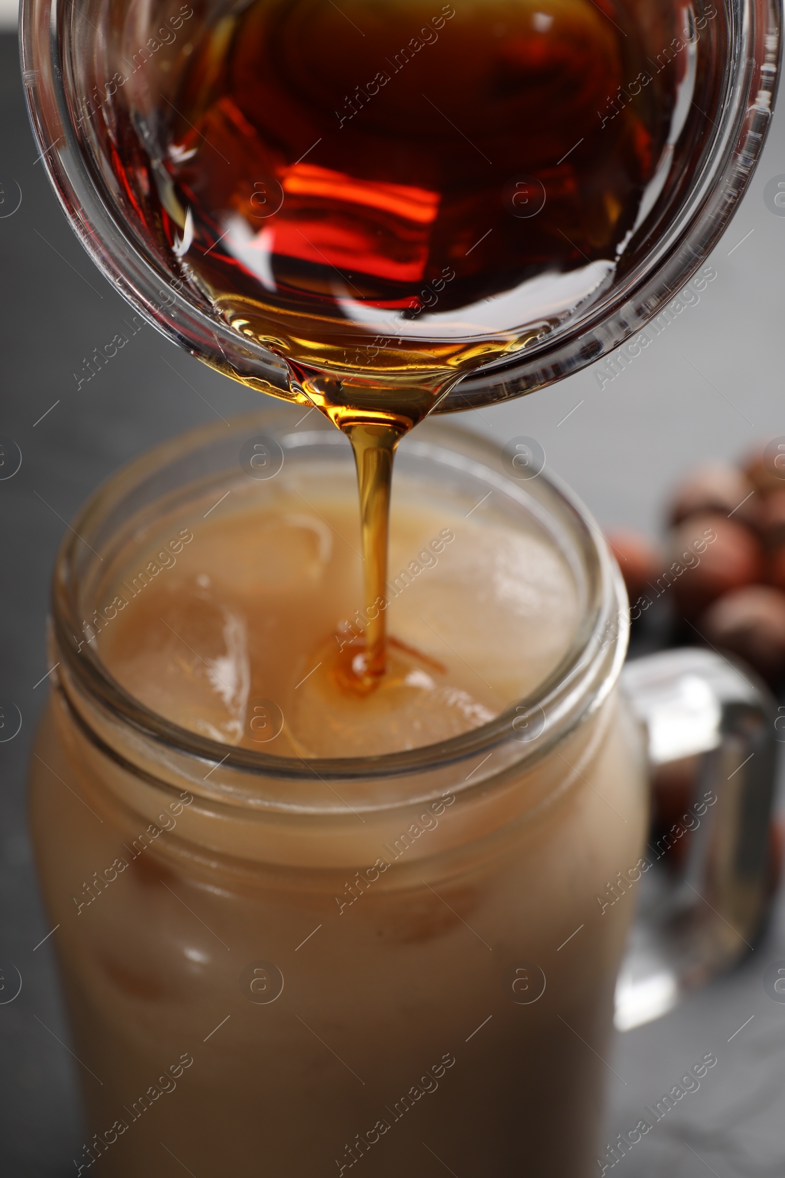 Photo of Pouring syrup into mason jar of tasty iced coffee on black table, closeup