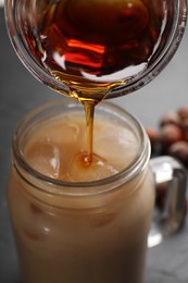 Photo of Pouring syrup into mason jar of tasty iced coffee on black table, closeup