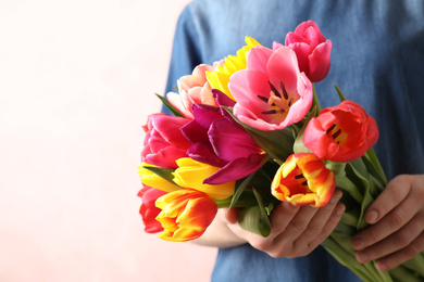 Photo of Woman holding beautiful spring tulips on light background, closeup