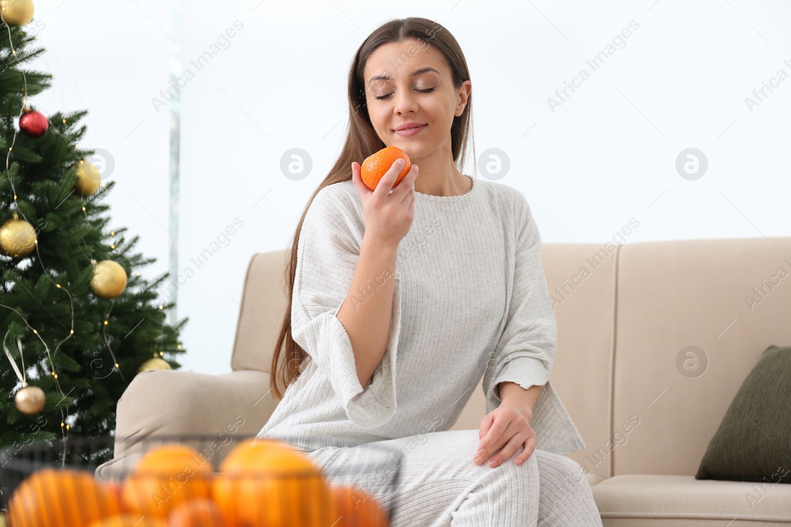 Photo of Woman with tangerine sitting on sofa near Christmas tree