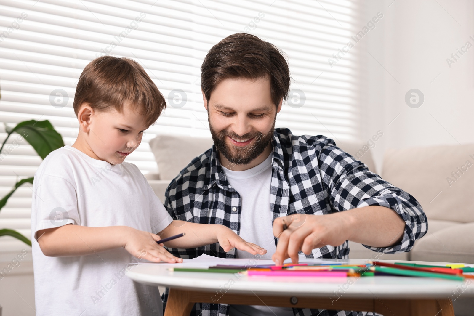 Photo of Happy dad and son drawing together at table indoors