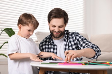 Happy dad and son drawing together at table indoors