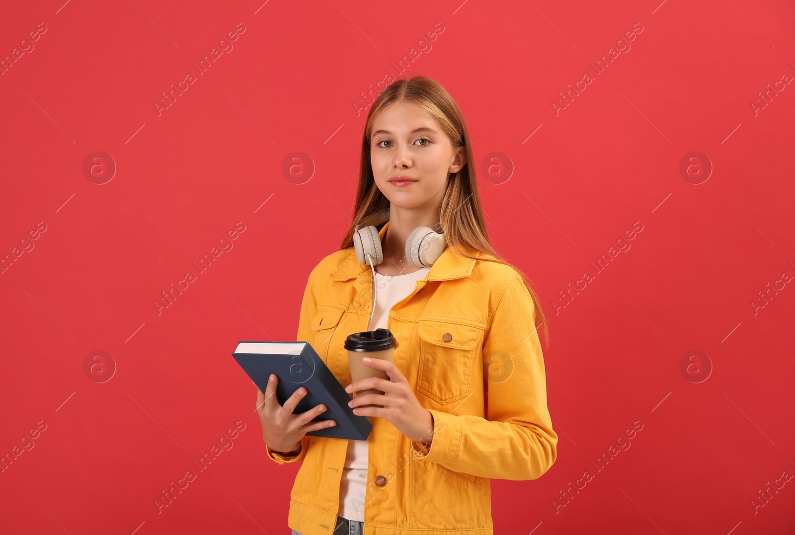 Photo of Teenage student with book, cup of coffee and headphones on red background