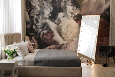 Beautiful room interior with large bed, mirror and floral pattern on wall