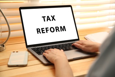Tax reform concept. Woman working with modern laptop at wooden table, closeup