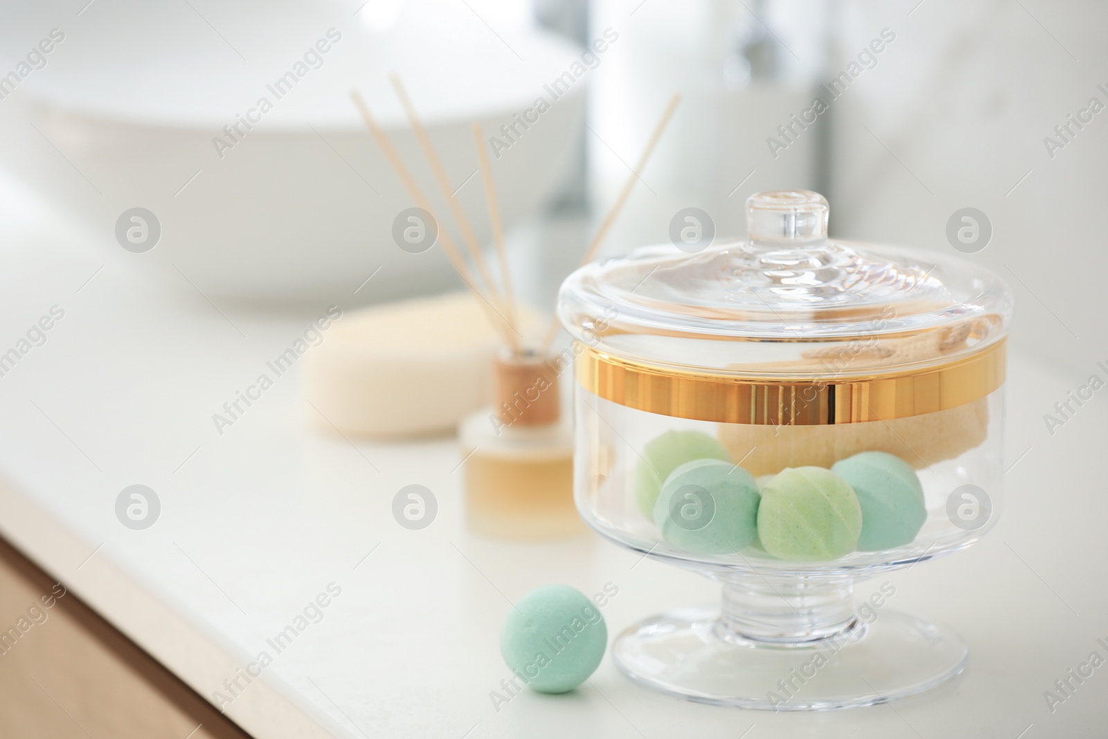 Photo of Jar with bath bombs and loofah sponge on white countertop in bathroom