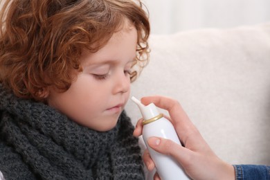 Mother using nasal spray to treat her little son on sofa, closeup