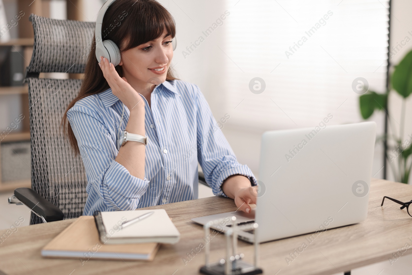 Photo of Woman in headphones watching webinar at wooden table in office