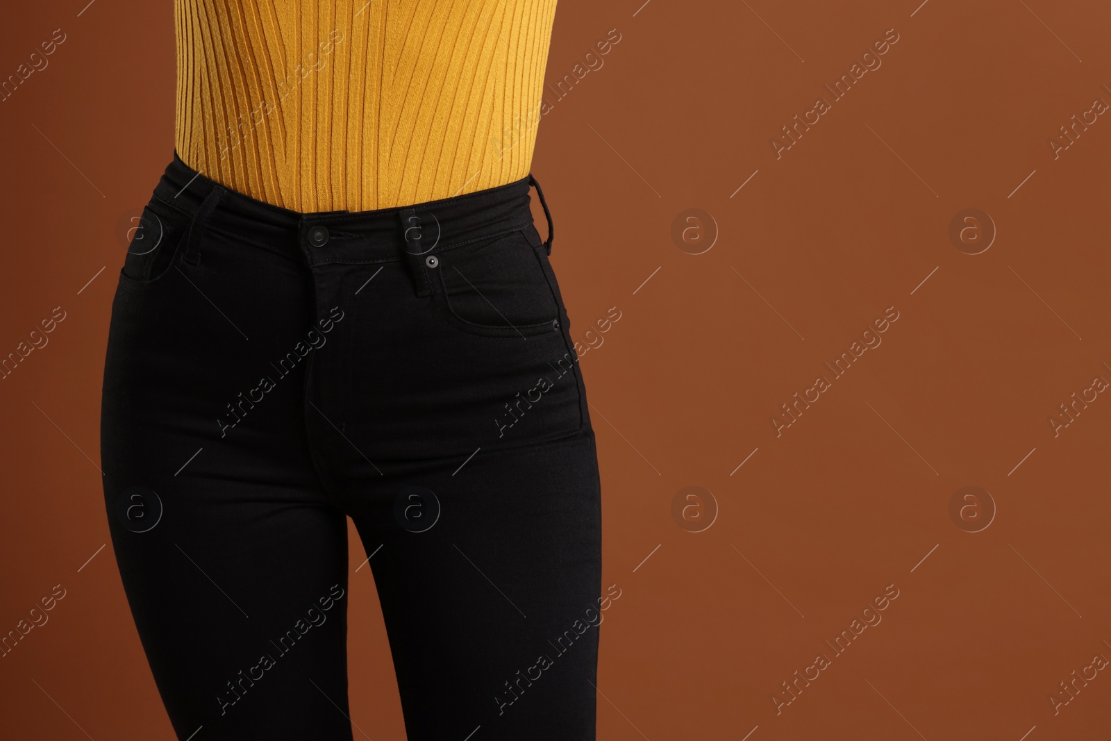 Photo of Woman wearing stylish black jeans on brown background, closeup. Space for text