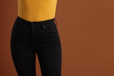 Woman wearing stylish black jeans on brown background, closeup. Space for text