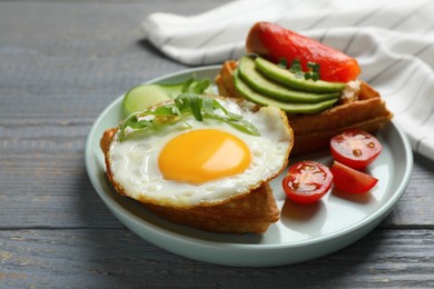 Photo of Delicious Belgian waffle with fried egg, arugula and vegetables on grey wooden table, closeup