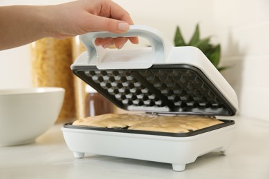 Woman closing modern Belgian waffle maker with dough in kitchen, closeup