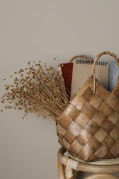 Photo of Stylish straw bag with beautiful dried flowers on chair near grey wall