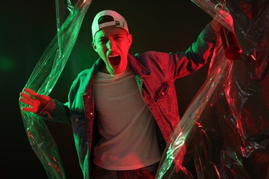 Young man with baseball bat on dark background in neon lights