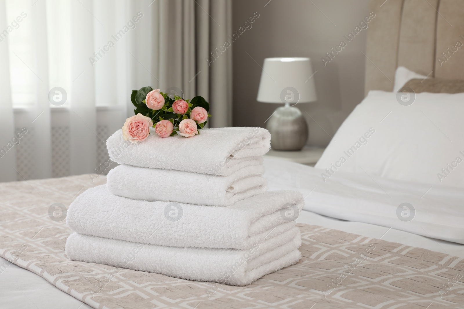 Photo of Stack of fresh towels with flowers on bed indoors, space for text