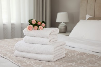 Stack of fresh towels with flowers on bed indoors, space for text