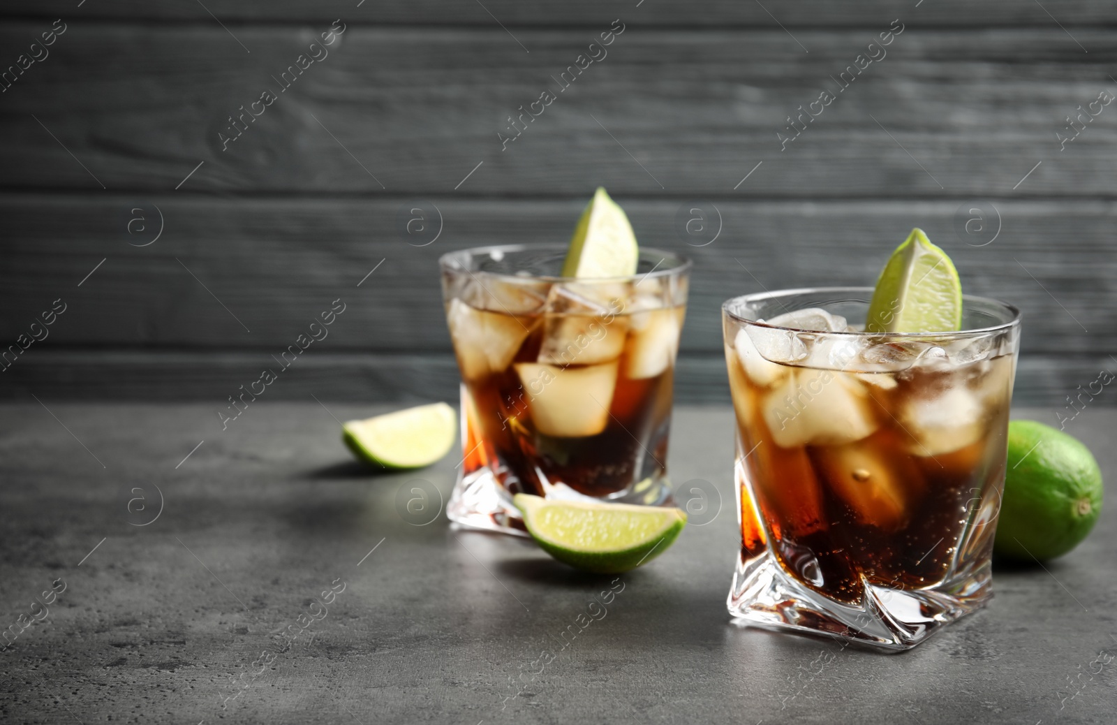 Photo of Glasses of cocktail with cola, ice and cut lime on table. Space for text