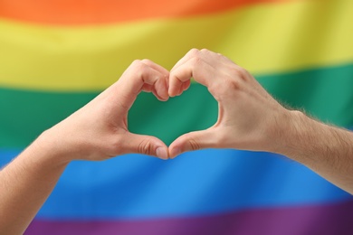 Photo of Gay couple making heart symbol with hands on rainbow background. Sexual minority
