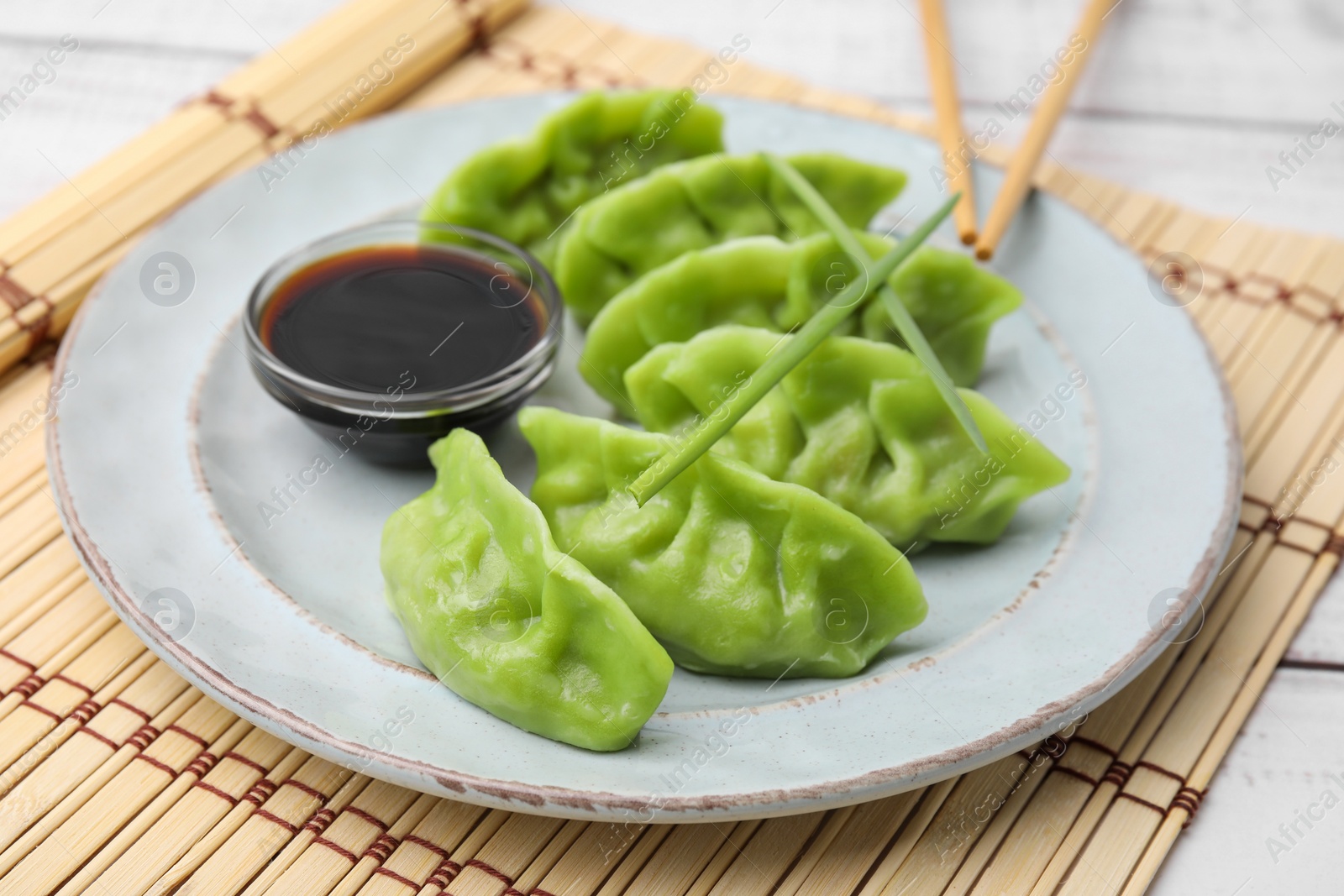 Photo of Delicious green dumplings (gyozas) and soy sauce on white table, closeup