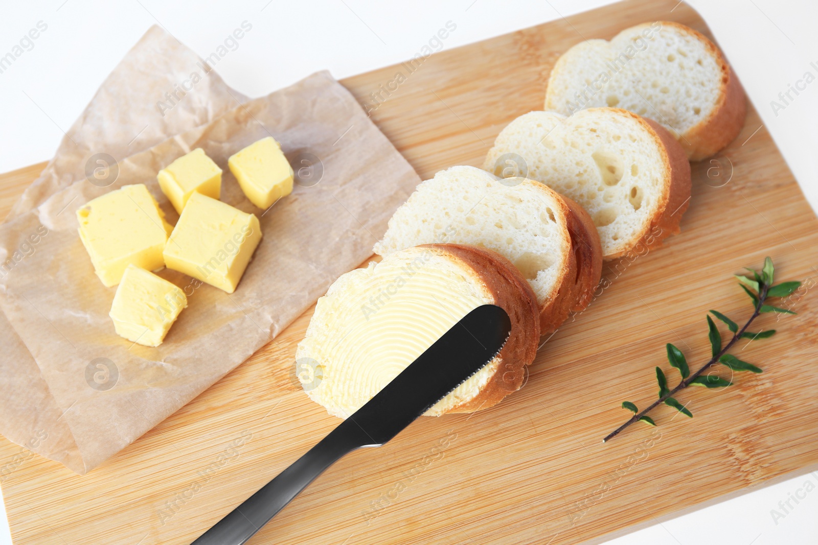 Photo of Wooden board with sliced baguette and fresh butter on white background, above view