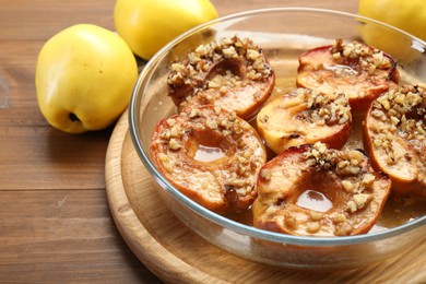 Tasty baked quinces with walnuts and honey in bowl on wooden table, closeup. Space for text