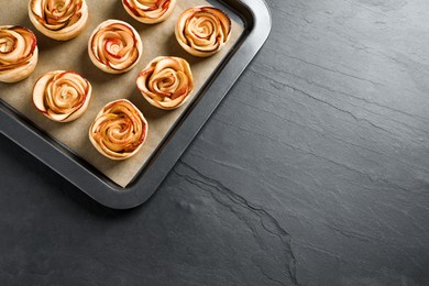 Photo of Tray with freshly baked apple roses on black table, top view. Space for text