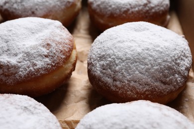 Photo of Delicious buns with powdered sugar on parchment paper, closeup