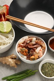 Photo of Black wok, spices and products on grey textured table, closeup