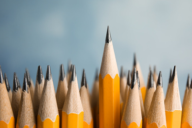 Photo of Many graphite pencils and one standing out on blue background, closeup