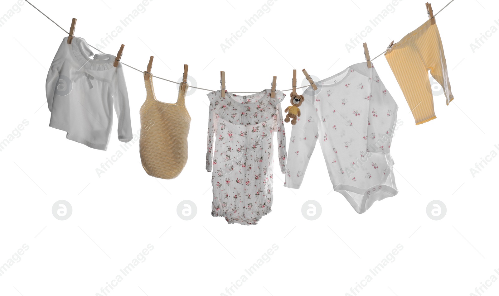 Photo of Different baby clothes and toy bear drying on laundry line against white background