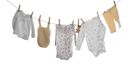 Photo of Different baby clothes and toy bear drying on laundry line against white background