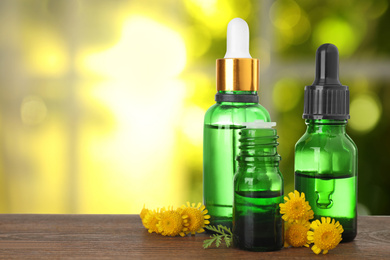 Bottles of essential oil and flowers on wooden table against blurred background. Space for text
