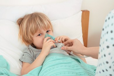 Mother helping her sick son with nebulizer inhalation in bedroom