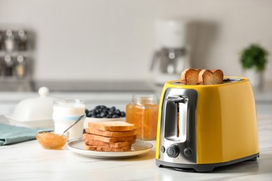 Photo of Yellow toaster with roasted bread slices, jam, blueberries and glass of milk on white marble table