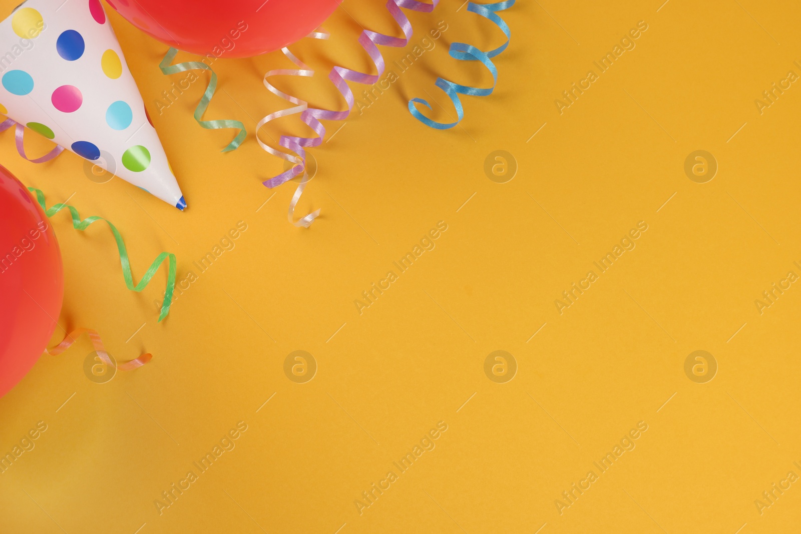 Photo of Colorful serpentine streamers, party hat and balloons on orange background, flat lay. Space for text