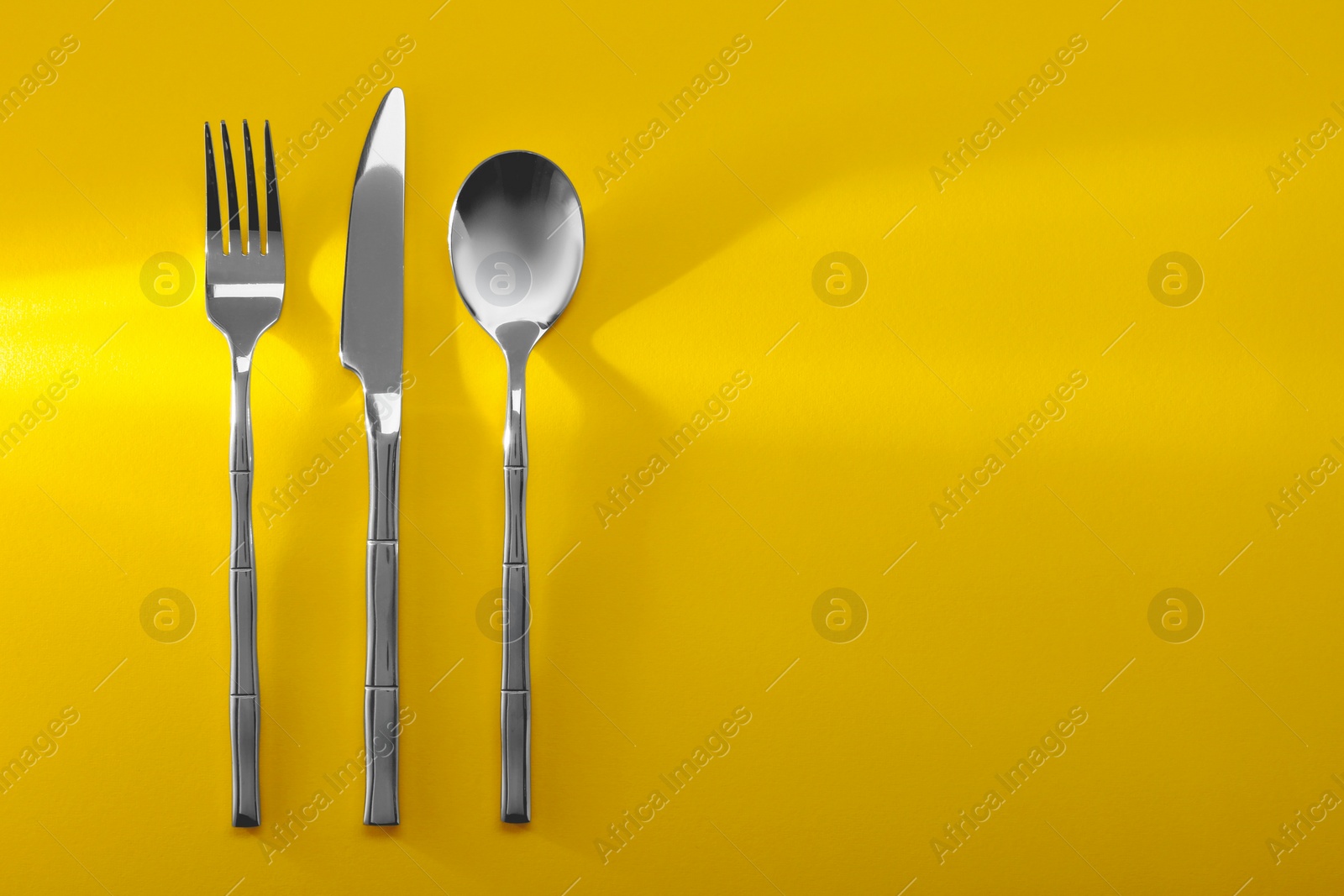 Photo of Spoon, fork and knife on yellow background, flat lay. Space for text