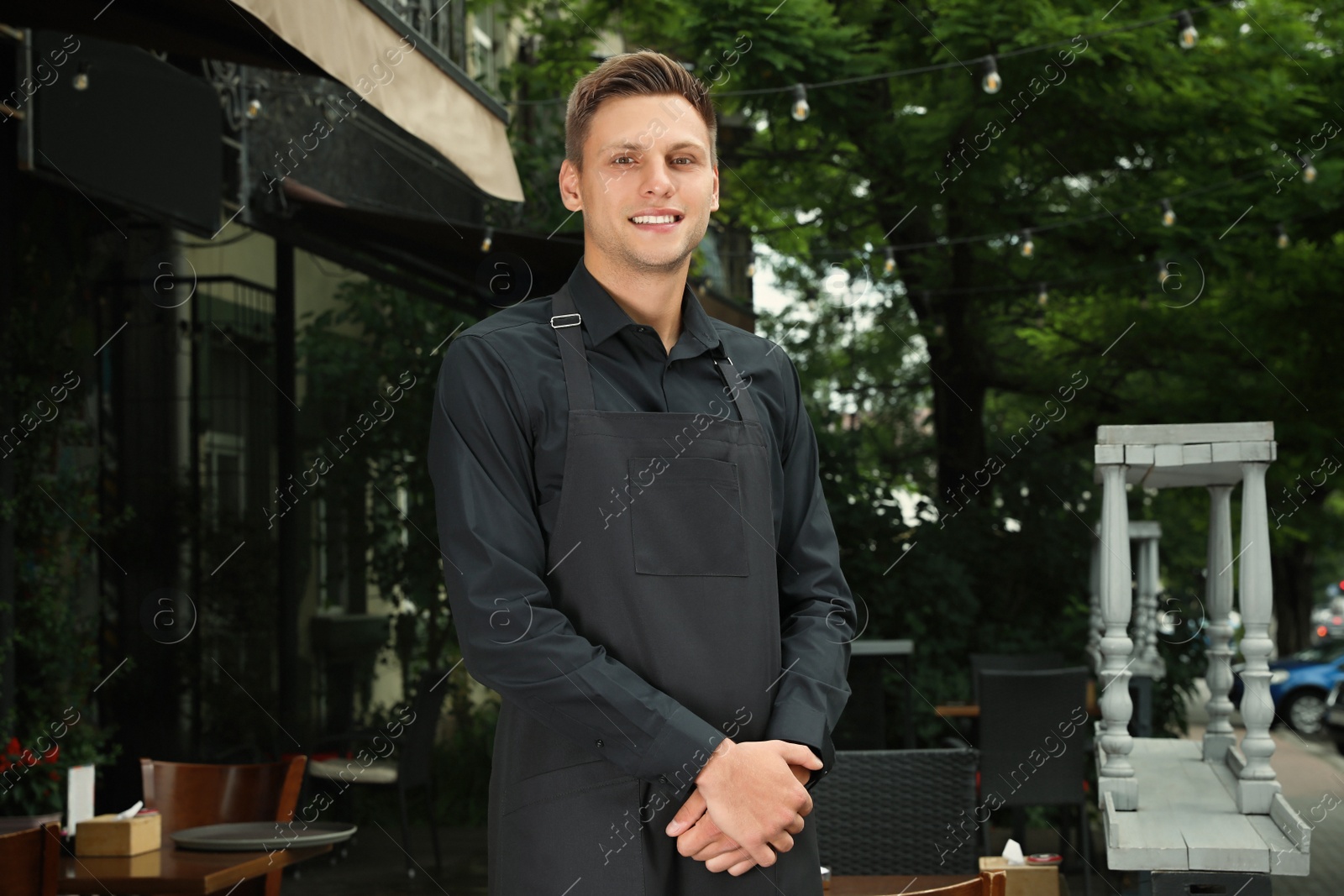 Photo of Happy young waiter in uniform near cafe