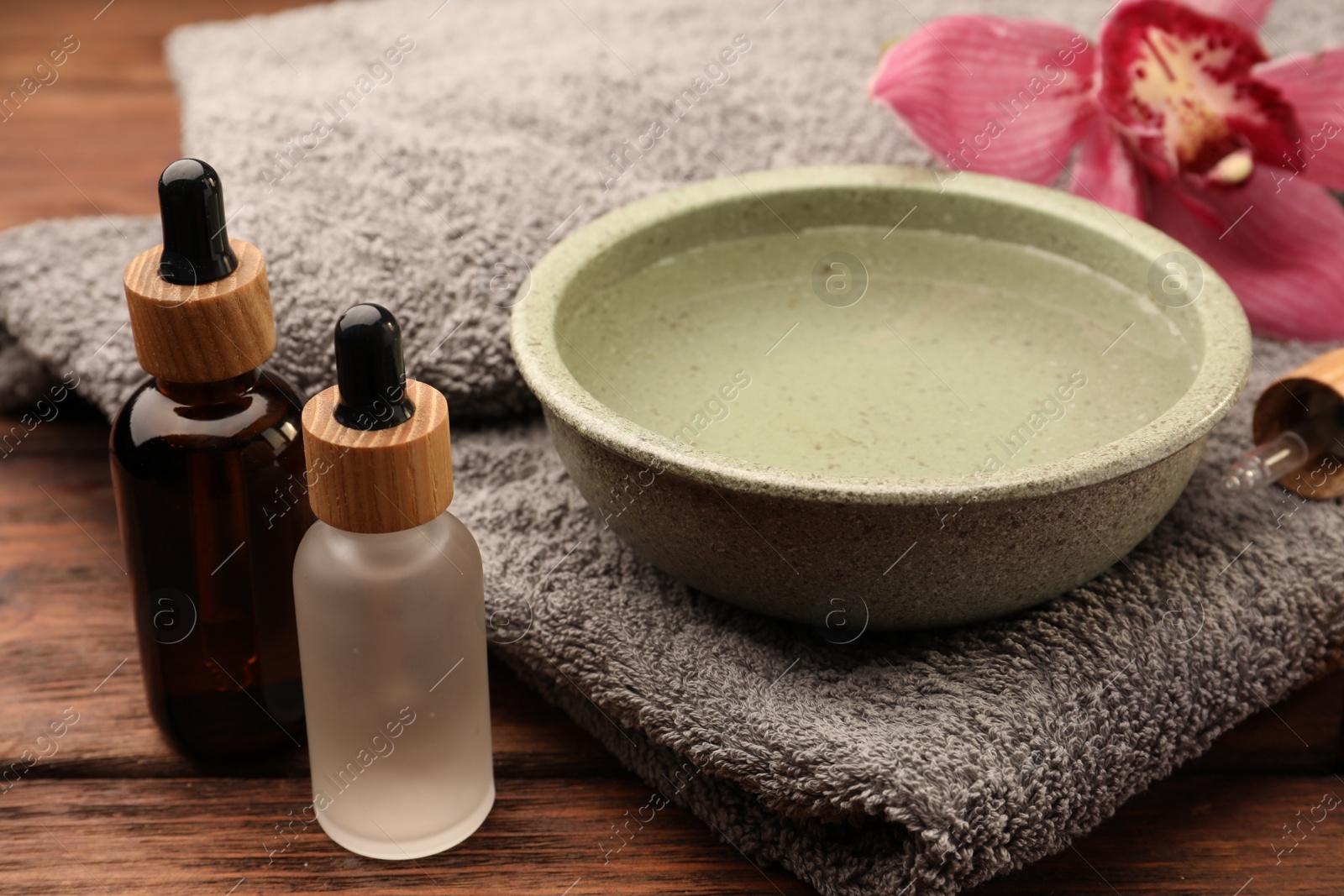 Photo of Bowl of essential oil and beautiful flower on wooden table. Aromatherapy treatment