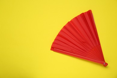 Bright red hand fan on yellow background, top view. Space for text