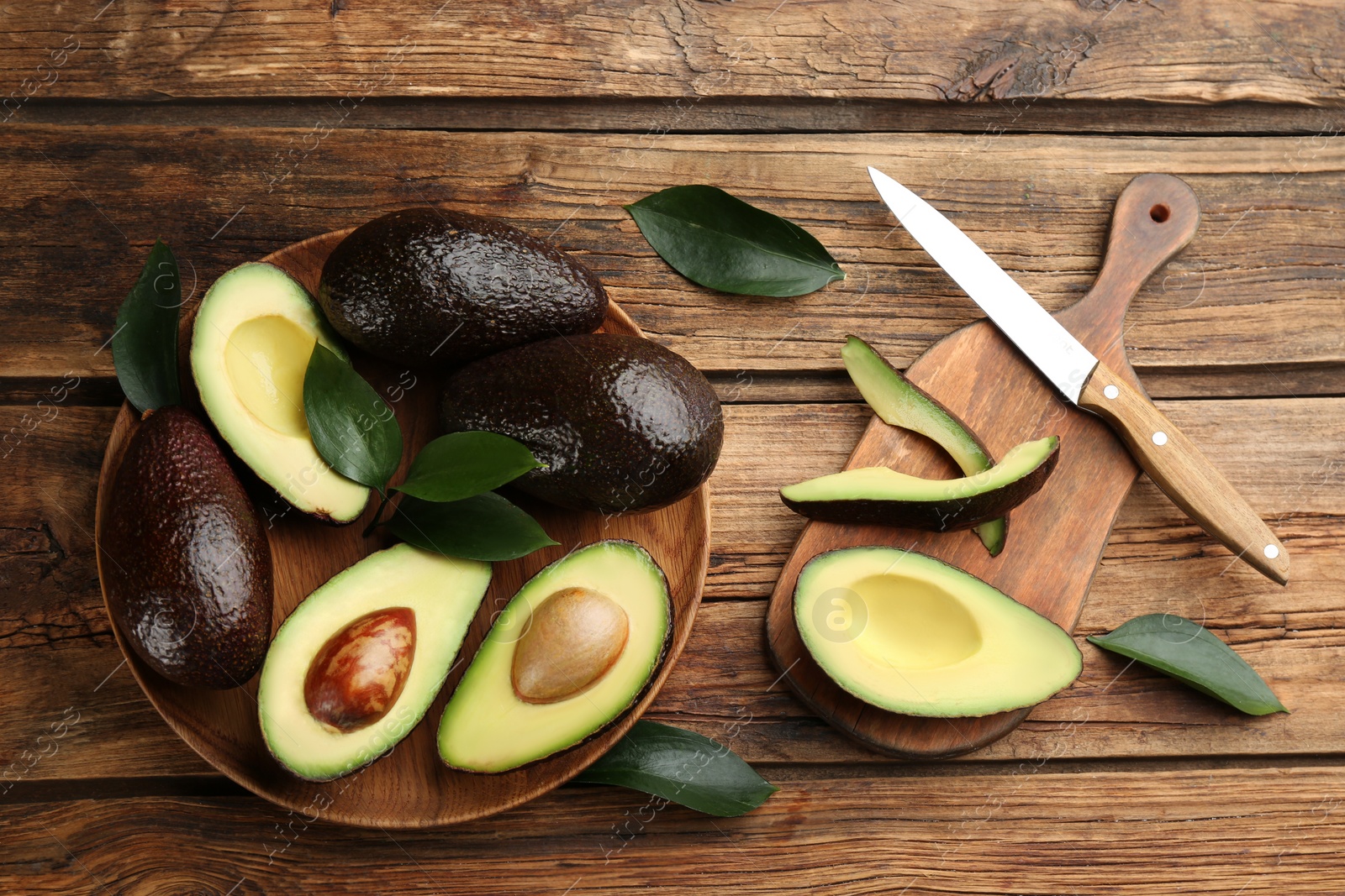 Photo of Whole and cut avocados on wooden table, flat lay