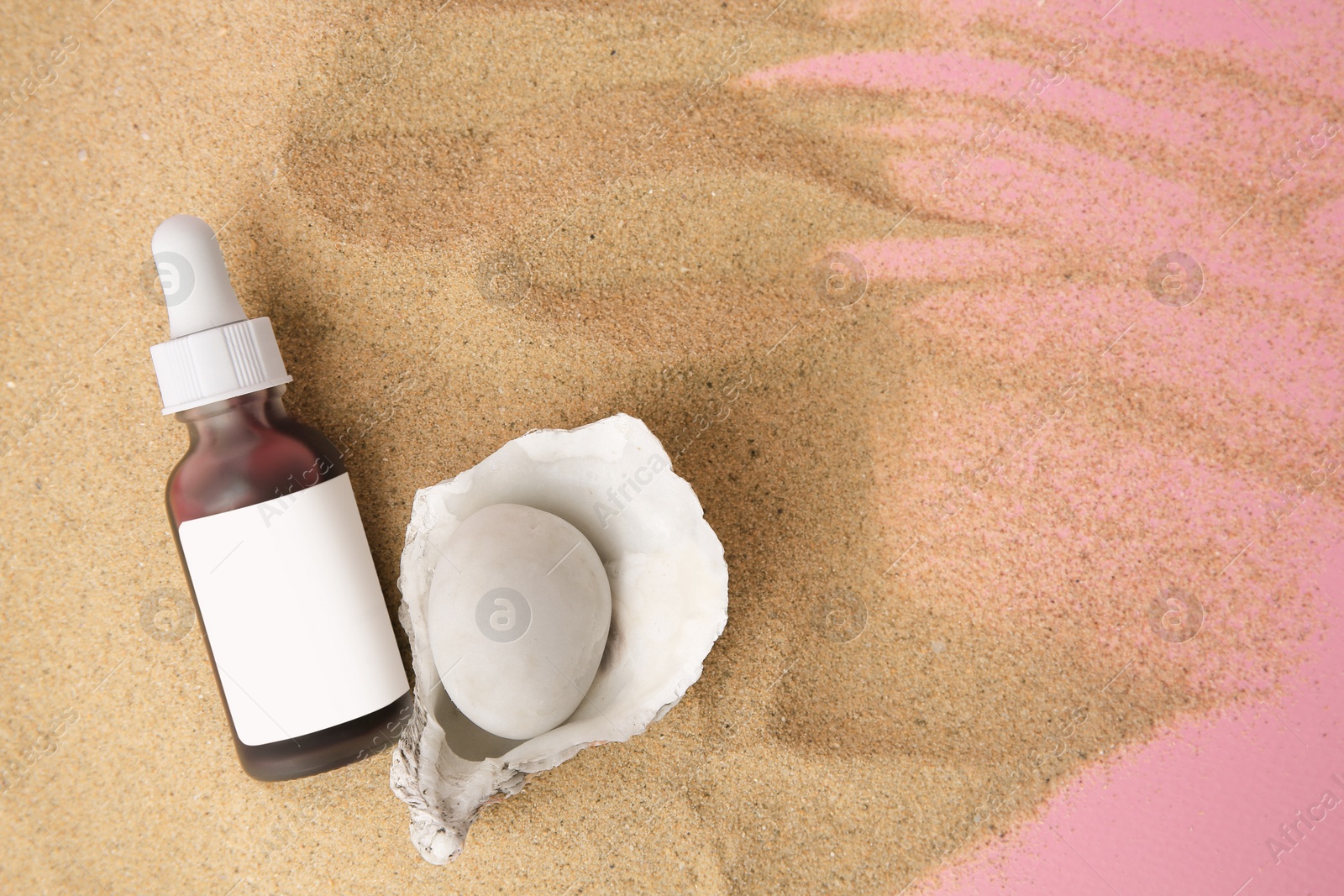 Photo of Bottle of serum, stone and seashell on sand against pink background, flat lay. Space for text