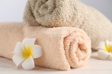 Photo of Closeup view of soft folded towels and plumeria flowers on white wooden table