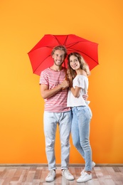 Couple with red umbrella near color wall