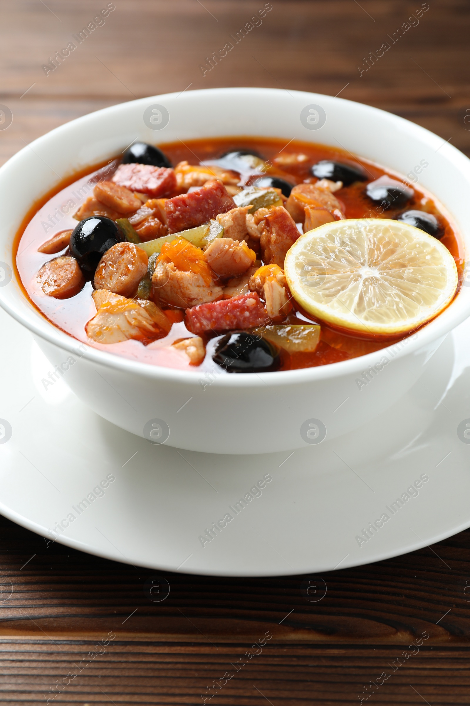 Photo of Meat solyanka soup with sausages, olives and vegetables on wooden table, closeup